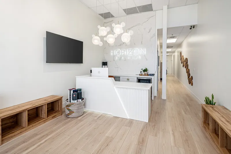 The Horizon Hot Yoga lobby: the front desk under the lit studio sign, benches and the hallway to the studios